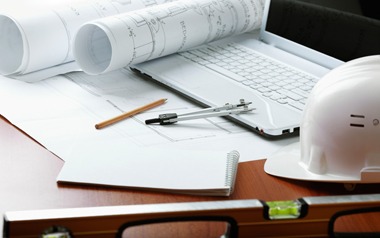 Desk with laptop, hard hat and building plans